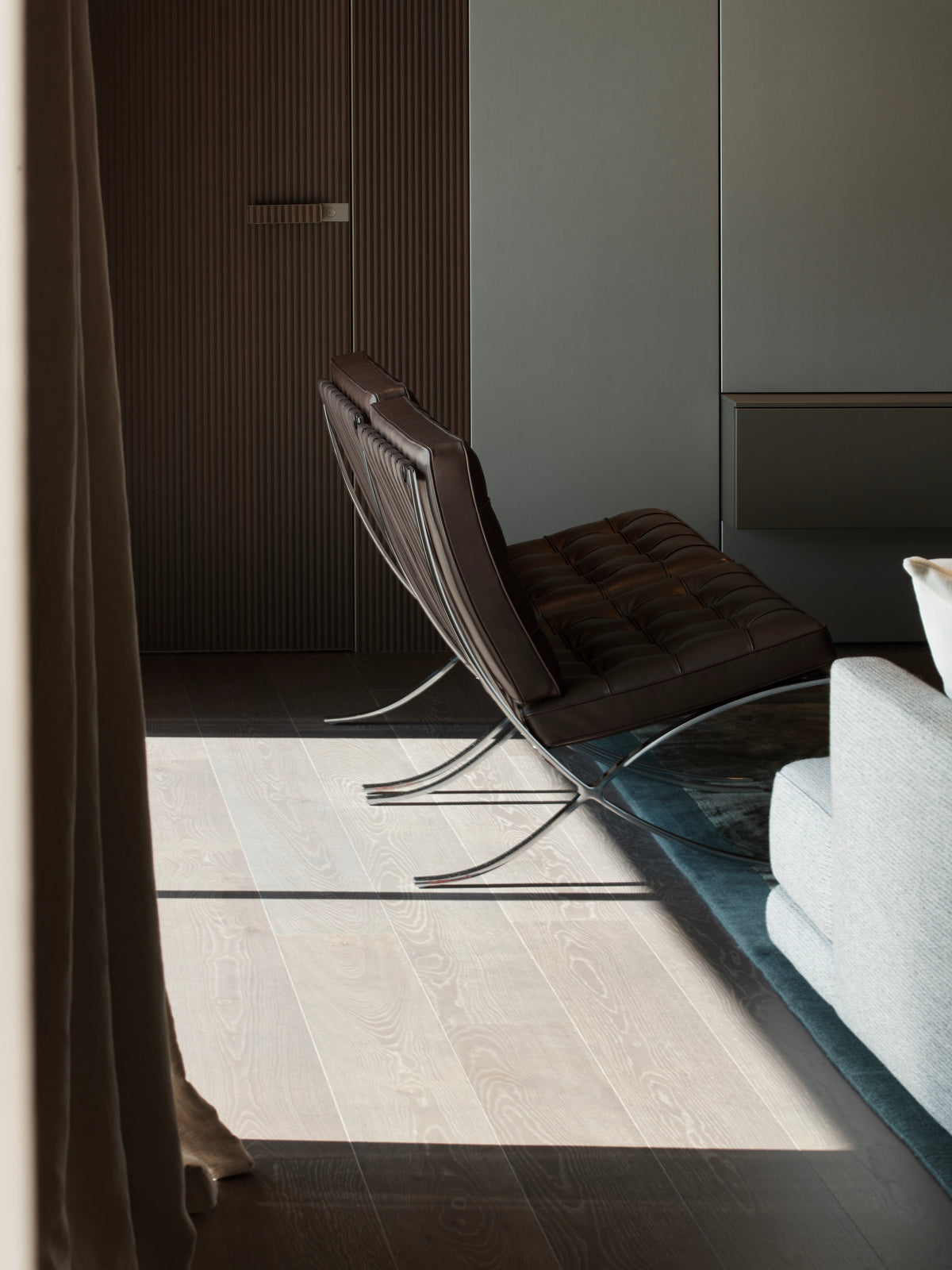 Dettaglio del living con poltrona di design, boiserie scura e luce naturale