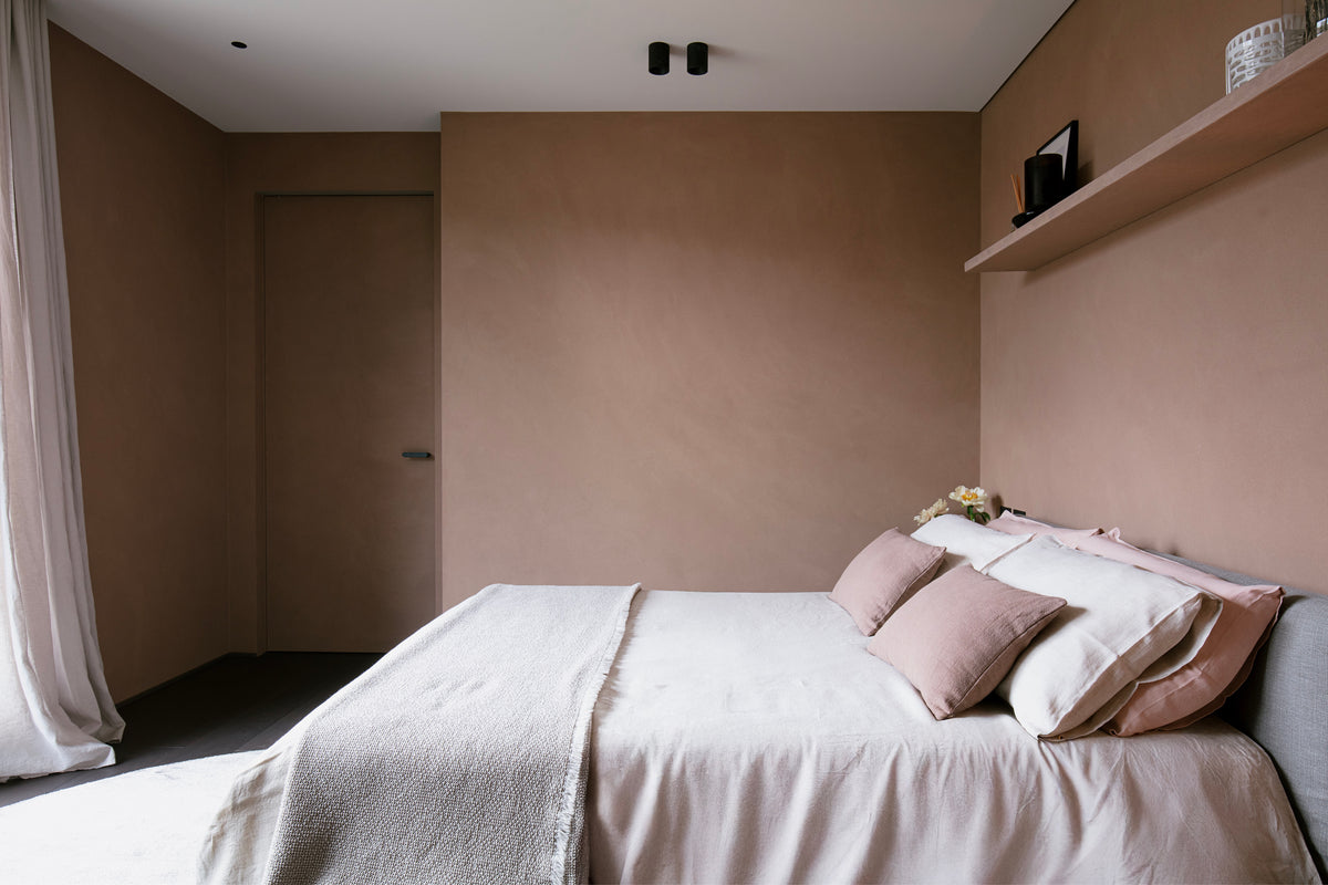 Camera minimal con letto tessile, mensola sospesa e pareti cipria