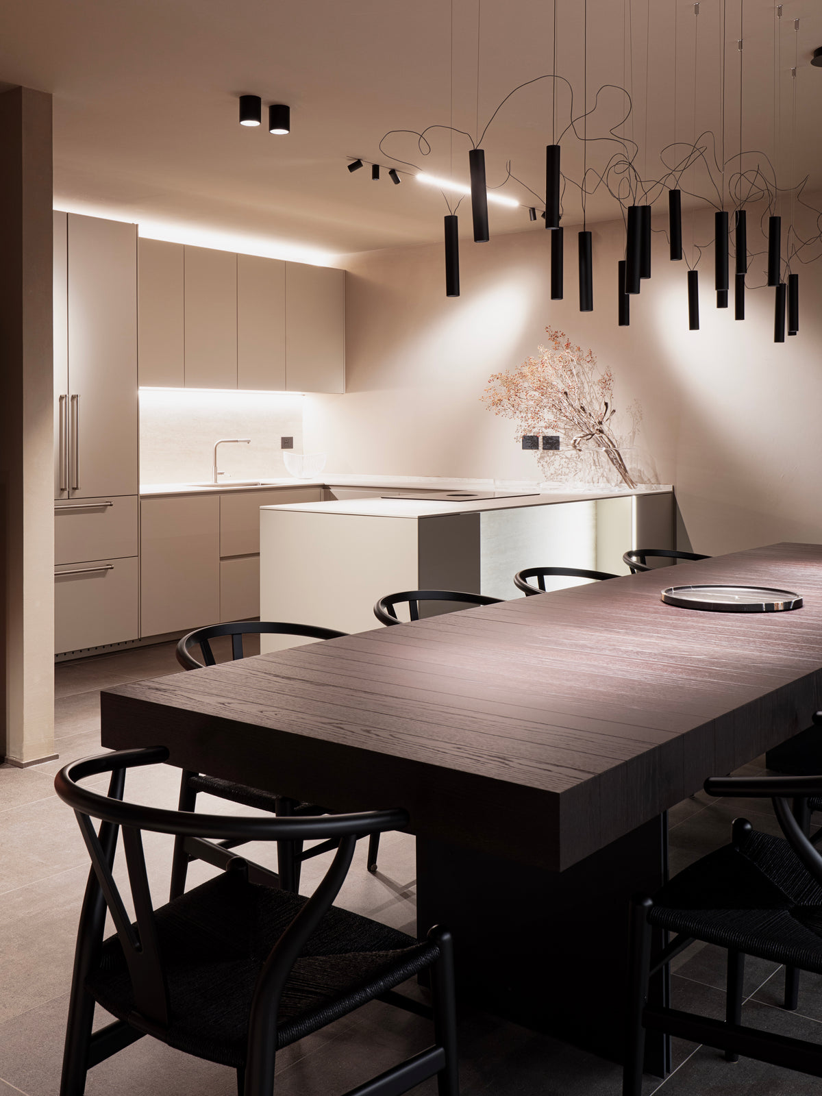 Taverna con tavolo in legno scuro, cucina minimale e sospensione scenografica