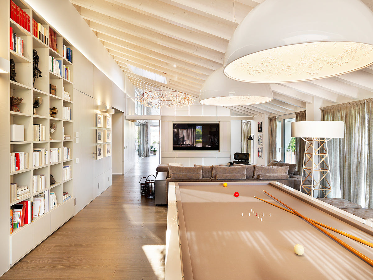 Open space dell’attico con tavolo da biliardo, libreria su misura e zona living sullo sfondo