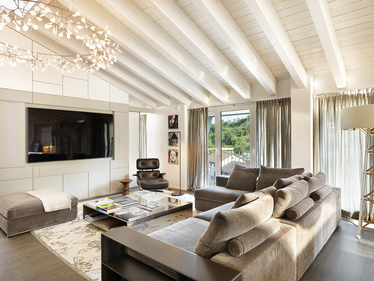 Zona living con divano componibile, poltrona lounge in pelle, parete TV con boiserie su progetto e grandi aperture verso l’esterno