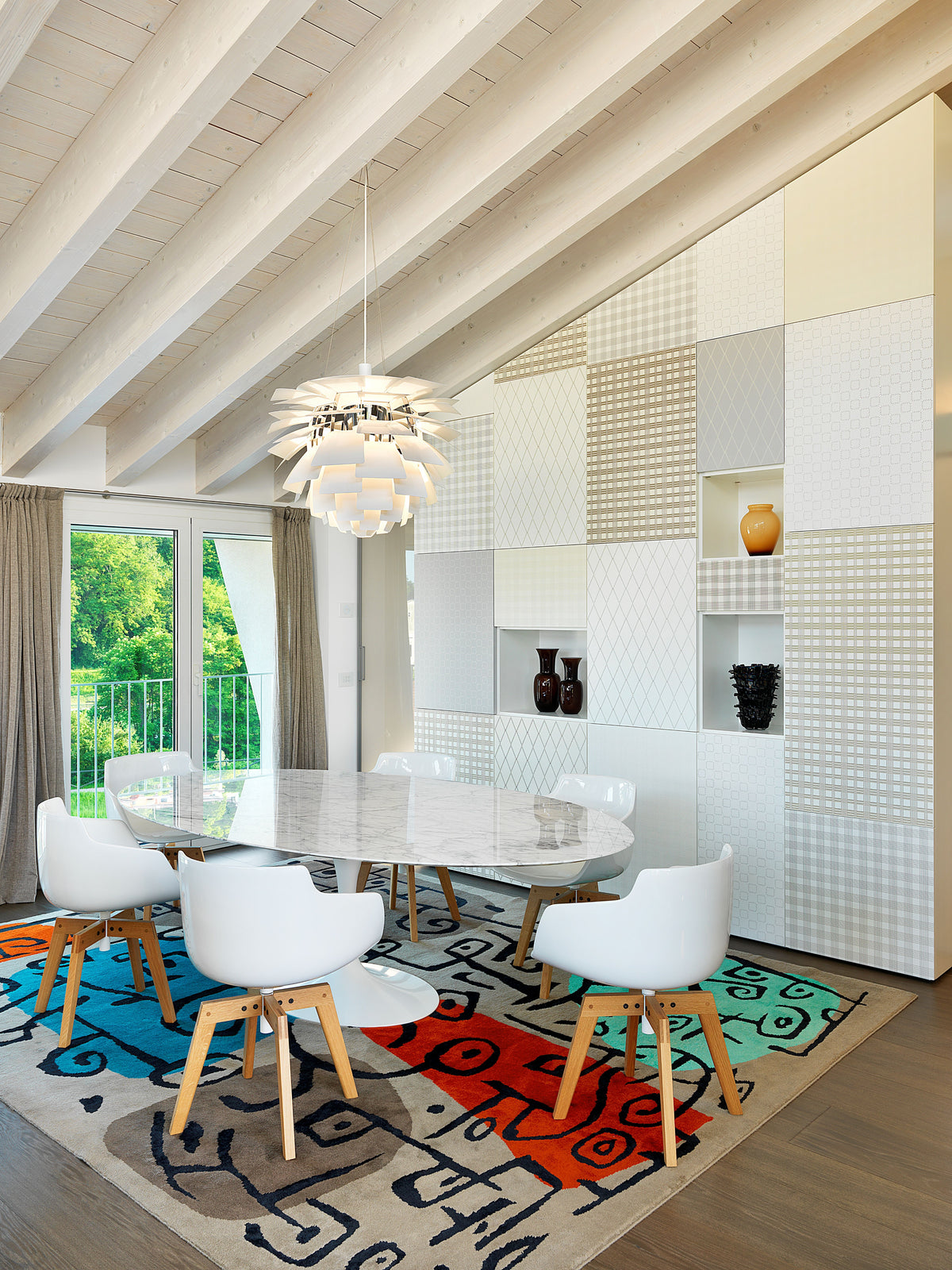 Zona pranzo con tavolo ovale, sedute con scocca bianca e gambe in legno, tappeto astratto e lampadario decorativo