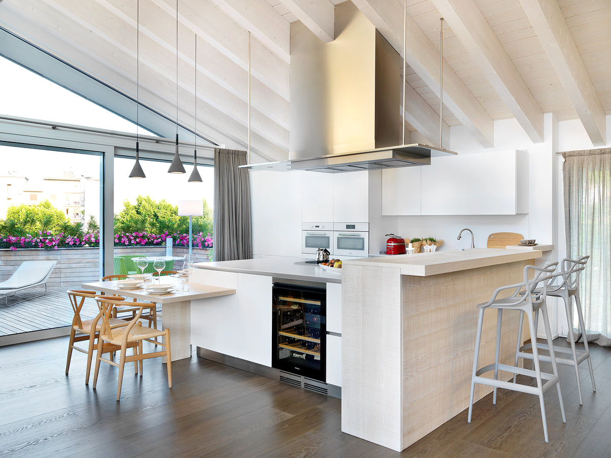Cucina con isola, tavoll integrato e bancone snack, con spazi fluidi tra preparazione, pranzo, living e relax outdoor