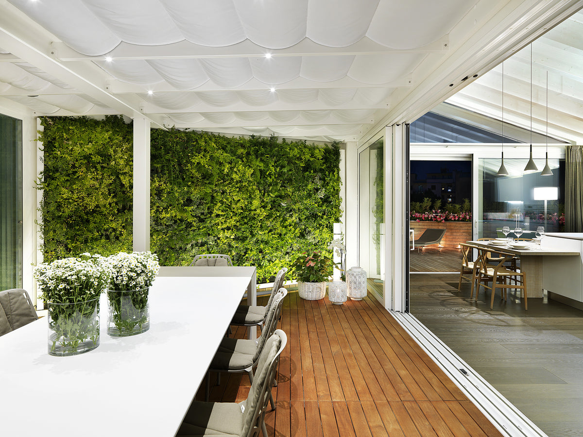 Zona pranzo esterna coperta con tavolo conviviale e parete verde verticale