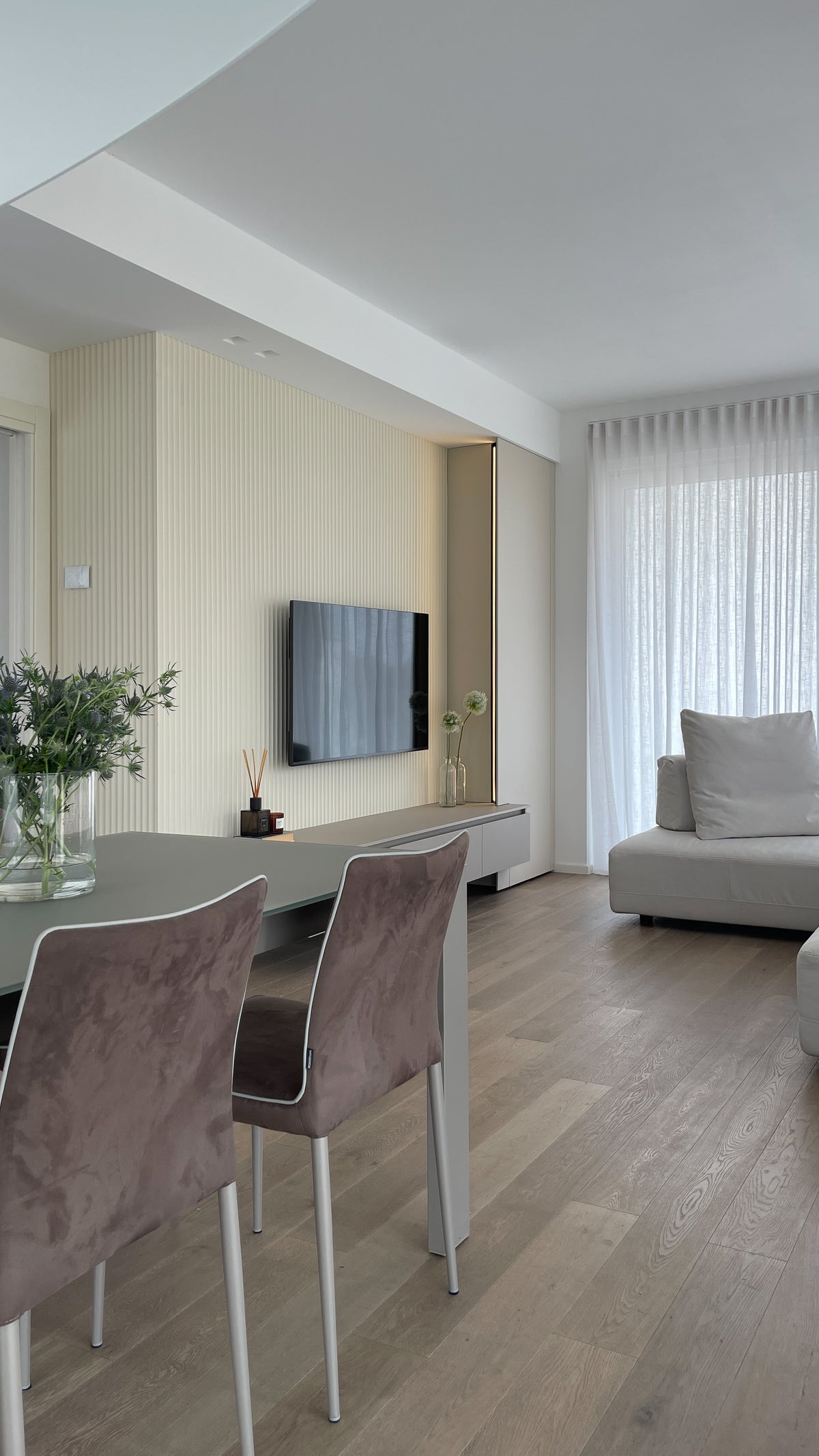 Open space con zona pranzo e living, parete TV su misura e arredi dai toni chiari