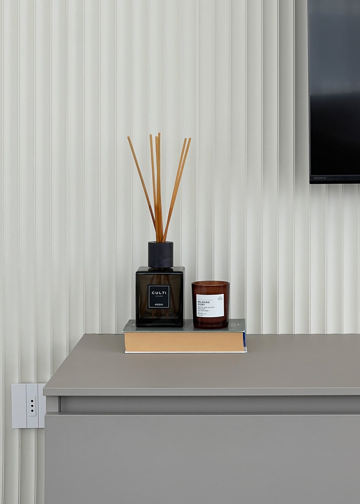 Dettaglio della parete TV con boiserie scanalata, mobile sospeso e complementi decorativi