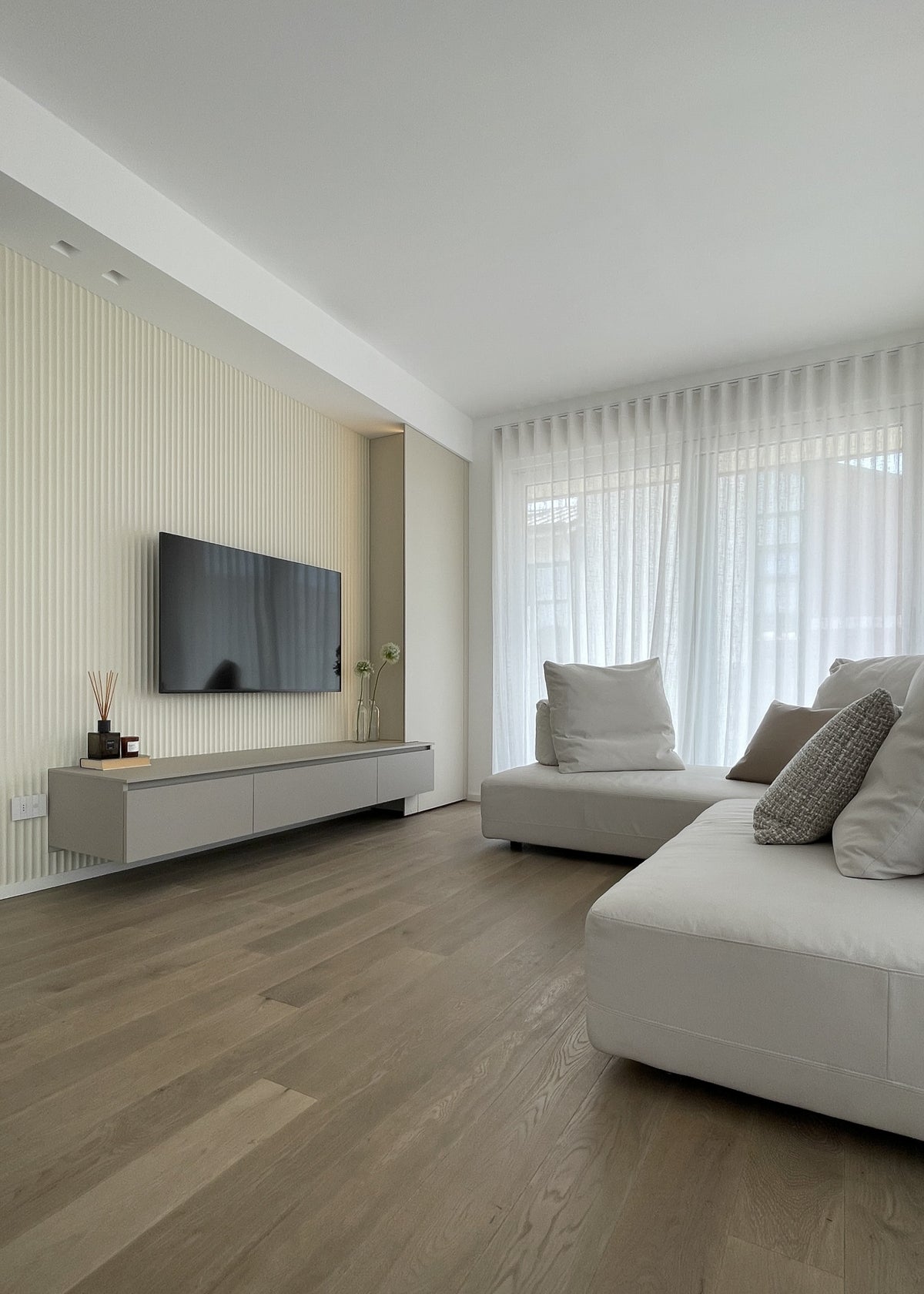 Interior design del living di un attico sul Lago di Garda con divano chiaro, boiserie TV e grandi vetrate