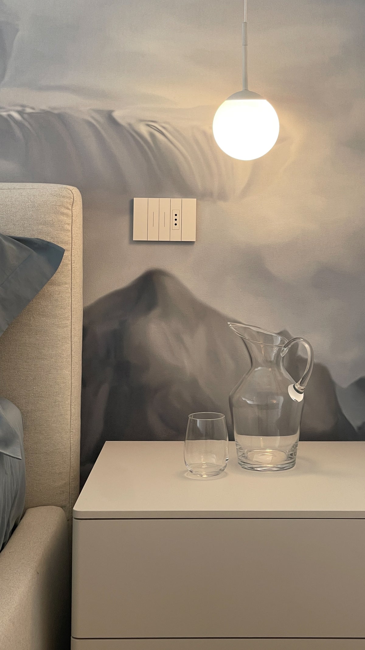 Dettaglio del comodino con lampada a sospensione davanti alla carta da parati decorativa della camera