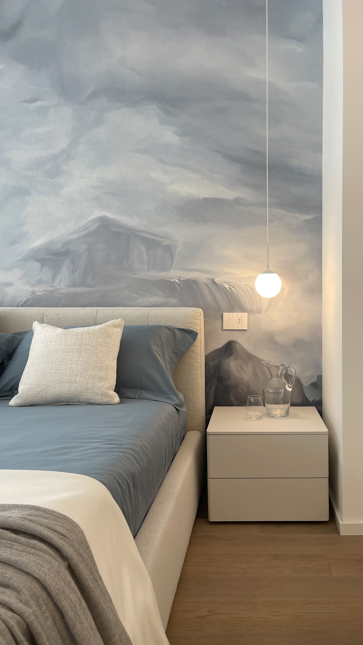 Letto imbottito con comodino bianco e carta da parati paesaggistica nella camera matrimoniale