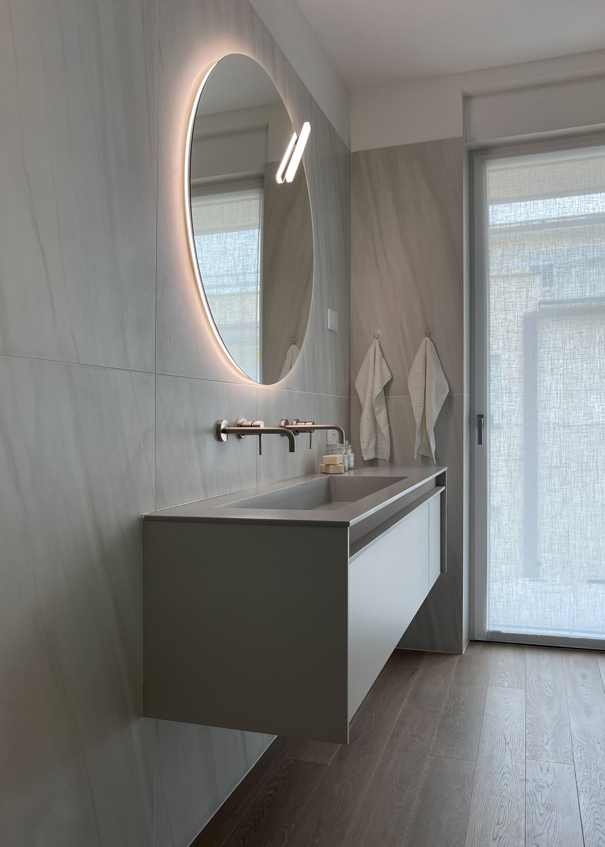 Bagno contemporaneo di attico sul Lago di Garda con mobile lavabo sospeso, grande specchio retroilluminato e superfici chiare