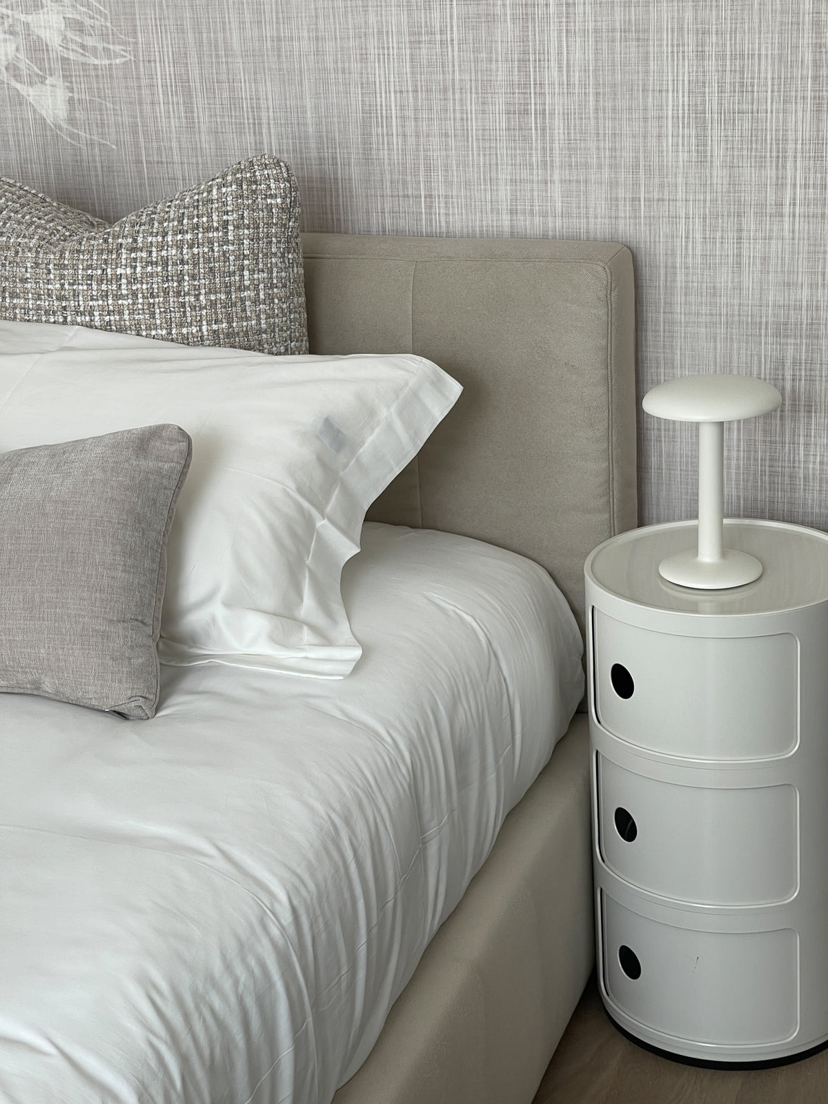 Dettaglio della seconda camera da letto con comodino cilindrico, lampada da tavolo e tessili neutri