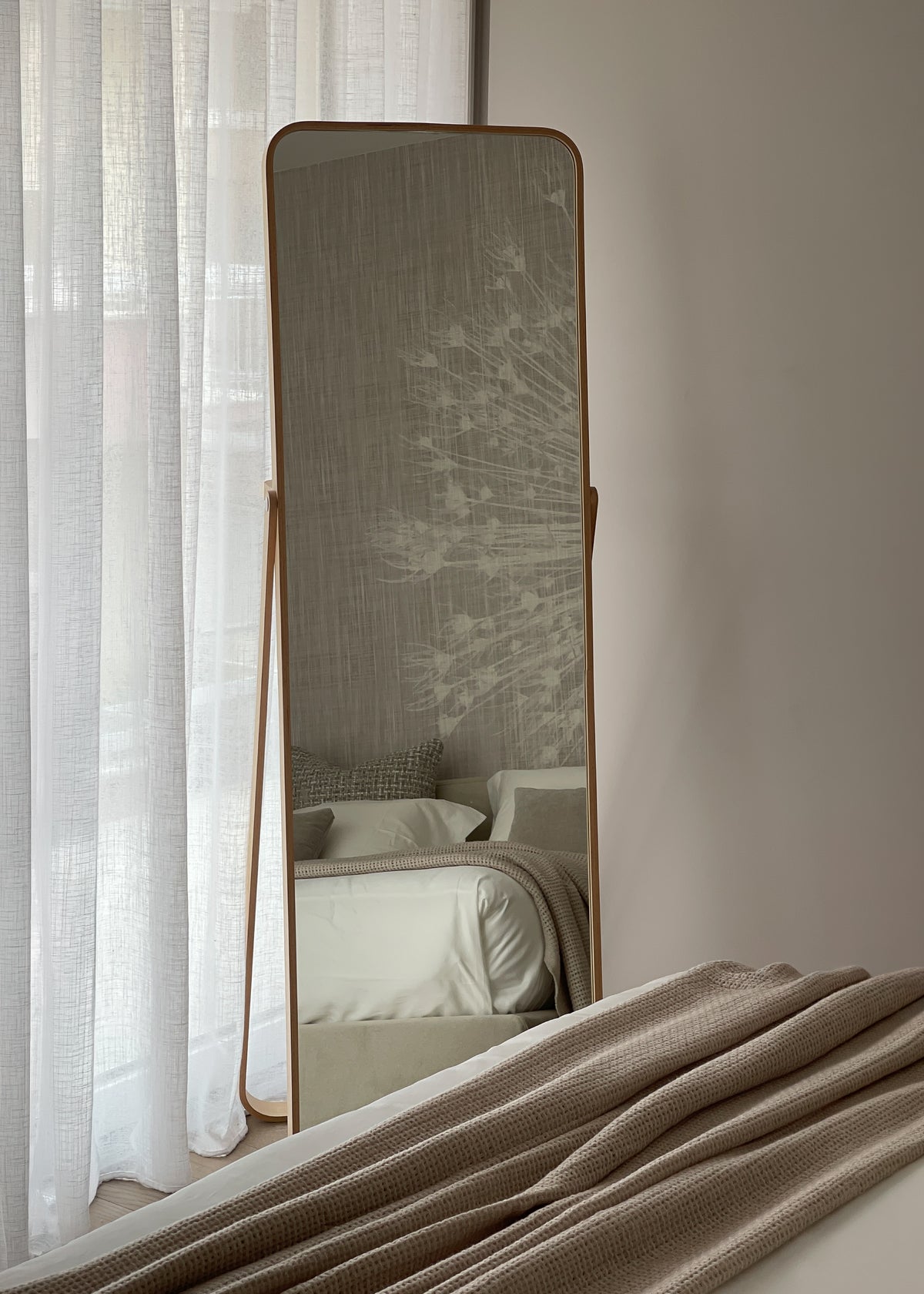 Specchio da terra nella camera da letto con riflesso della carta da parati decorativa e del letto