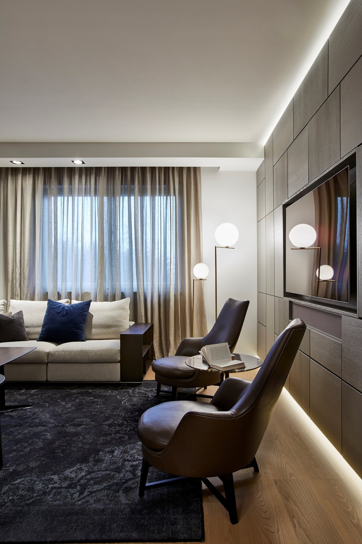 Living con poltrone in pelle, boiserie attrezzata e illuminazione integrata, progetto di interior design su misura