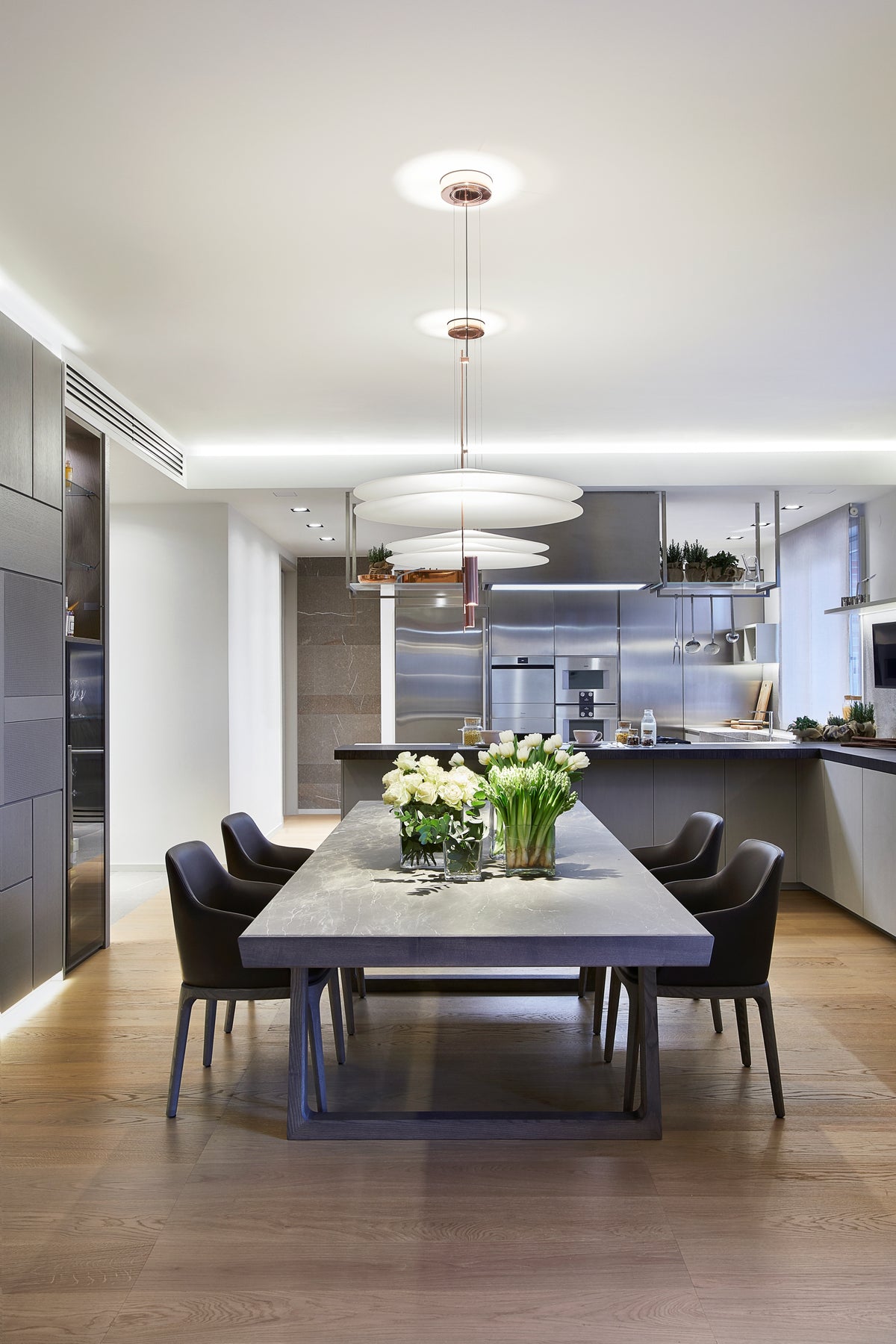 Zona pranzo contemporanea con tavolo materico, lampade sospese e cucina open space