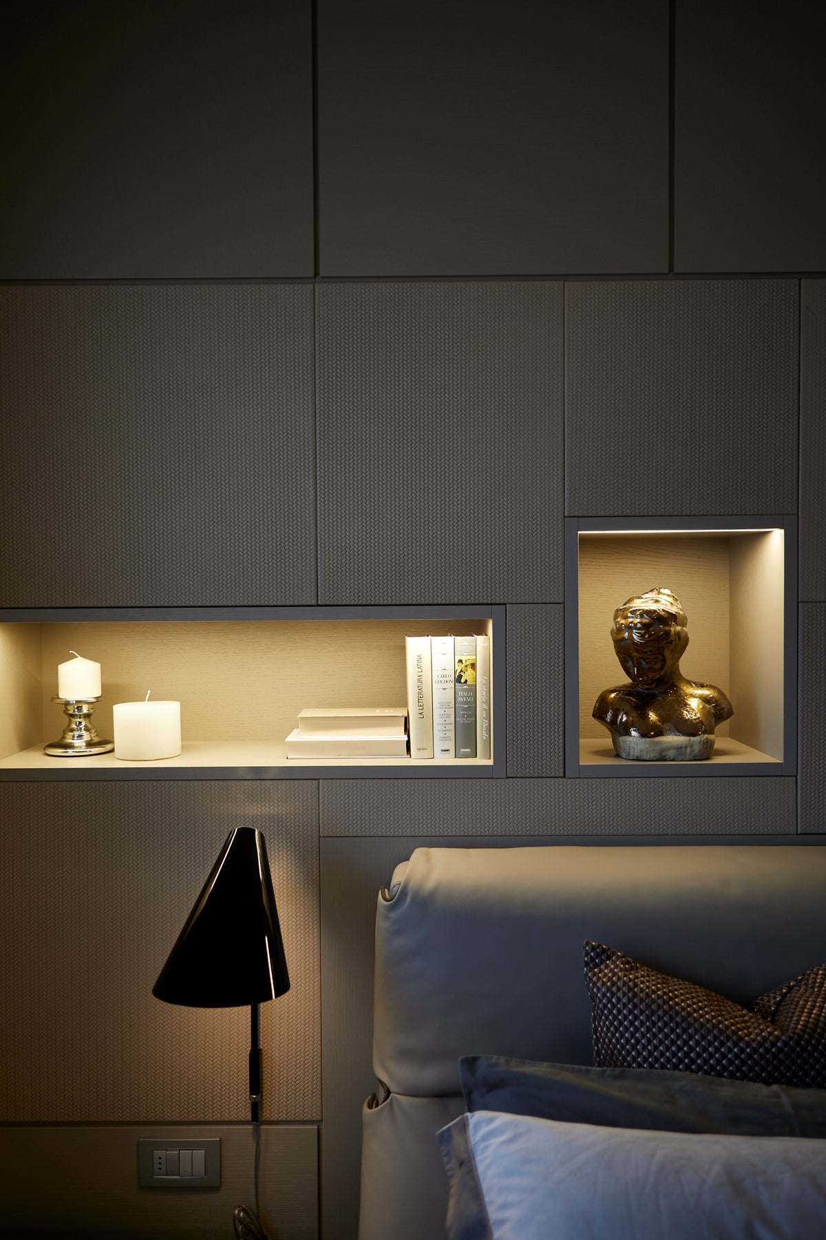 Parete attrezzata in camera da letto con nicchie illuminate, applique da comodino e finiture tessili della boiserie
