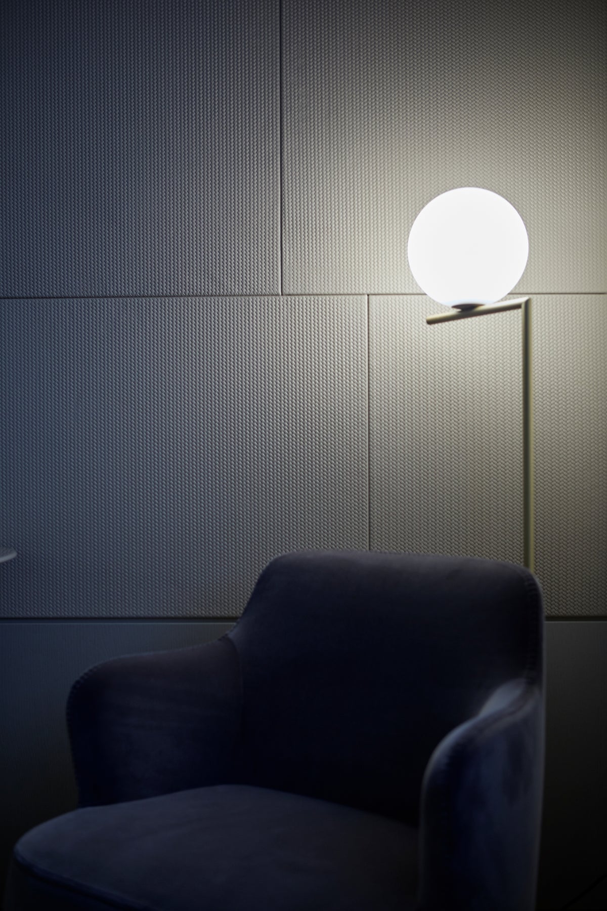 Dettaglio della poltrona imbottita della camera padronale con lampada da terra di design e boiserie con finitura tessile