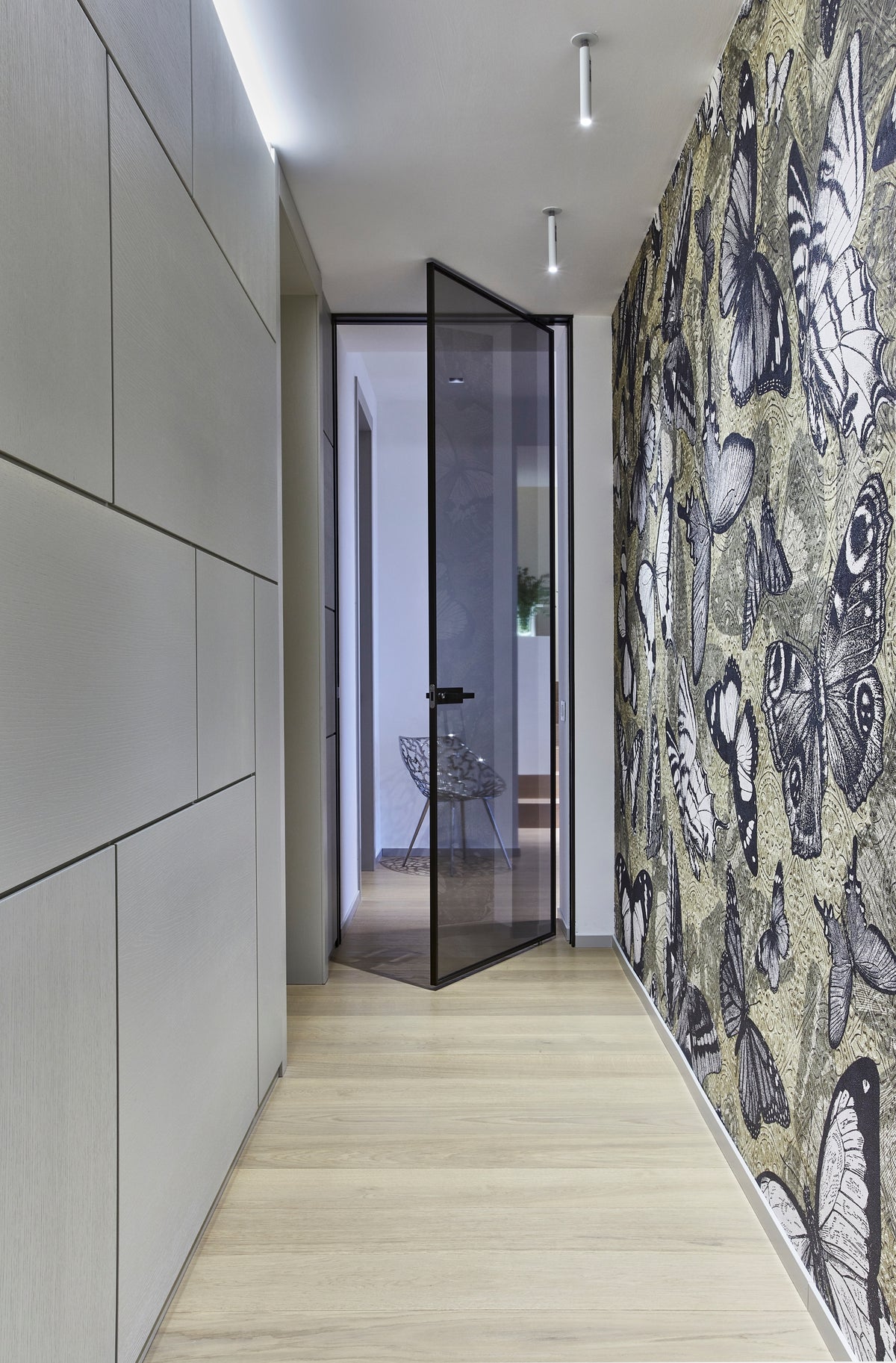 Corridoio zona notte con pannellature materiche, porta a bilico in vetro fumé e parete decorativa a tema naturale