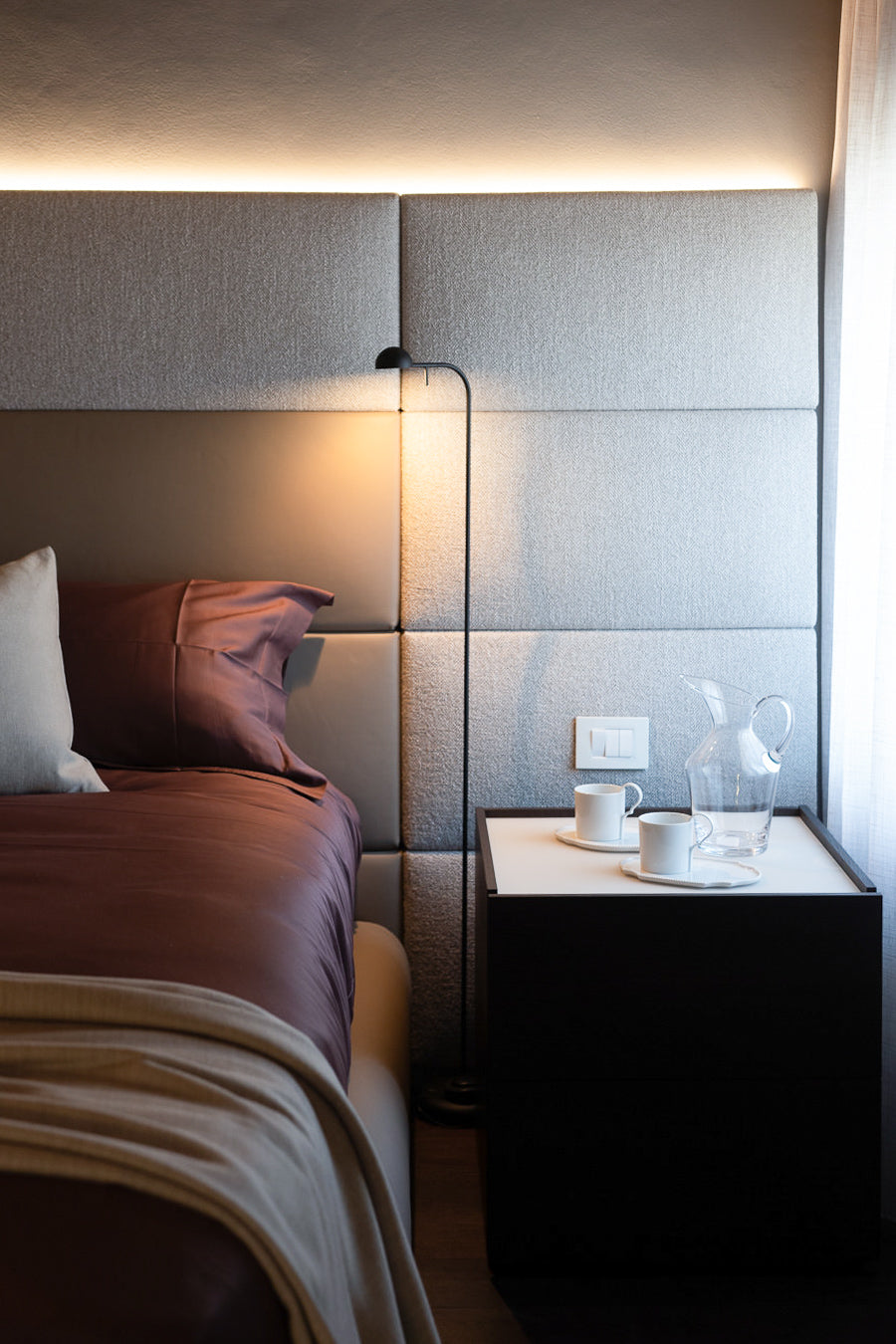 Dettaglio camera da letto con letto tessile con boiserie imbottita e comodino scuro