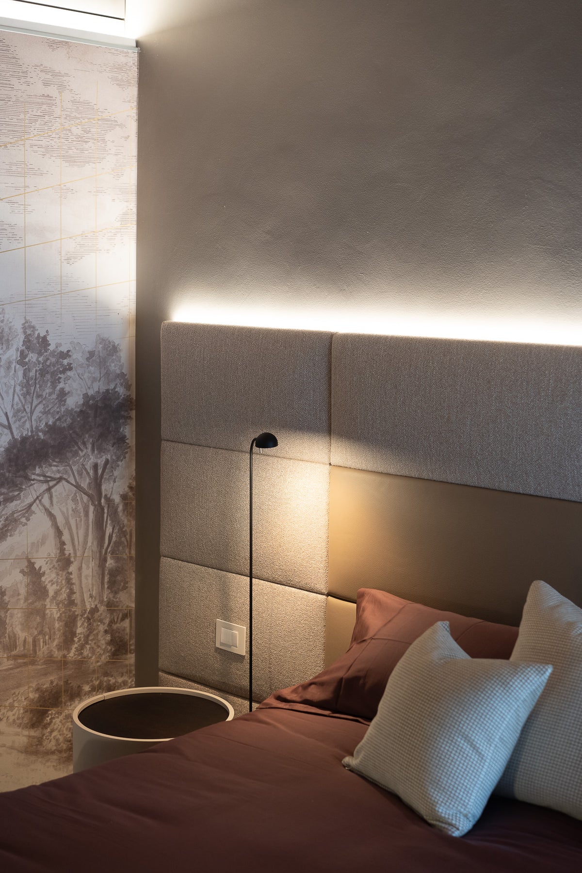 Dettaglio camera da letto con parete decorativa e letto tessile con boiserie imbottita
