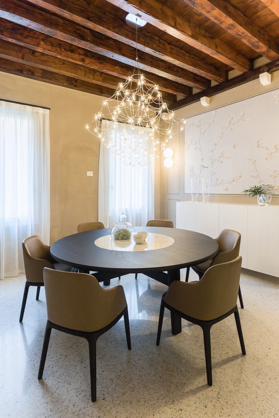 Zona pranzo con tavolo rotondo in legno scuro con elemento centrale in marmo e sedute imbottite in pelle