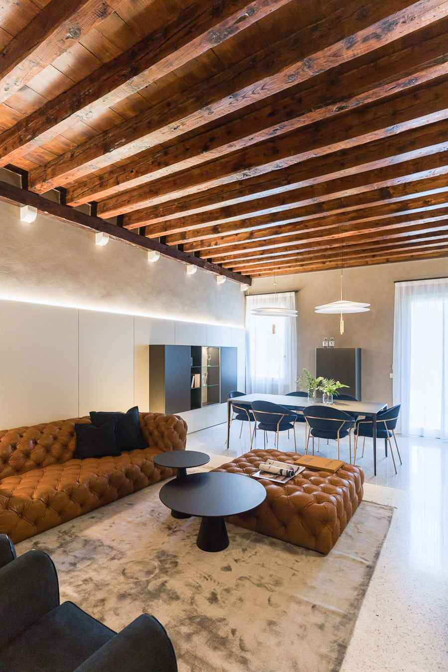 Zona giorno con divano capitonné, armadiatura a parete su misura e soffitto in legno a vista
