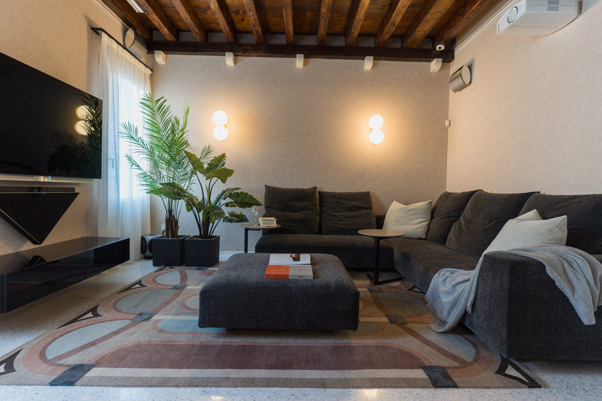 Area TV separata con divano grigio, pouf centrale e atmosfera raccolta