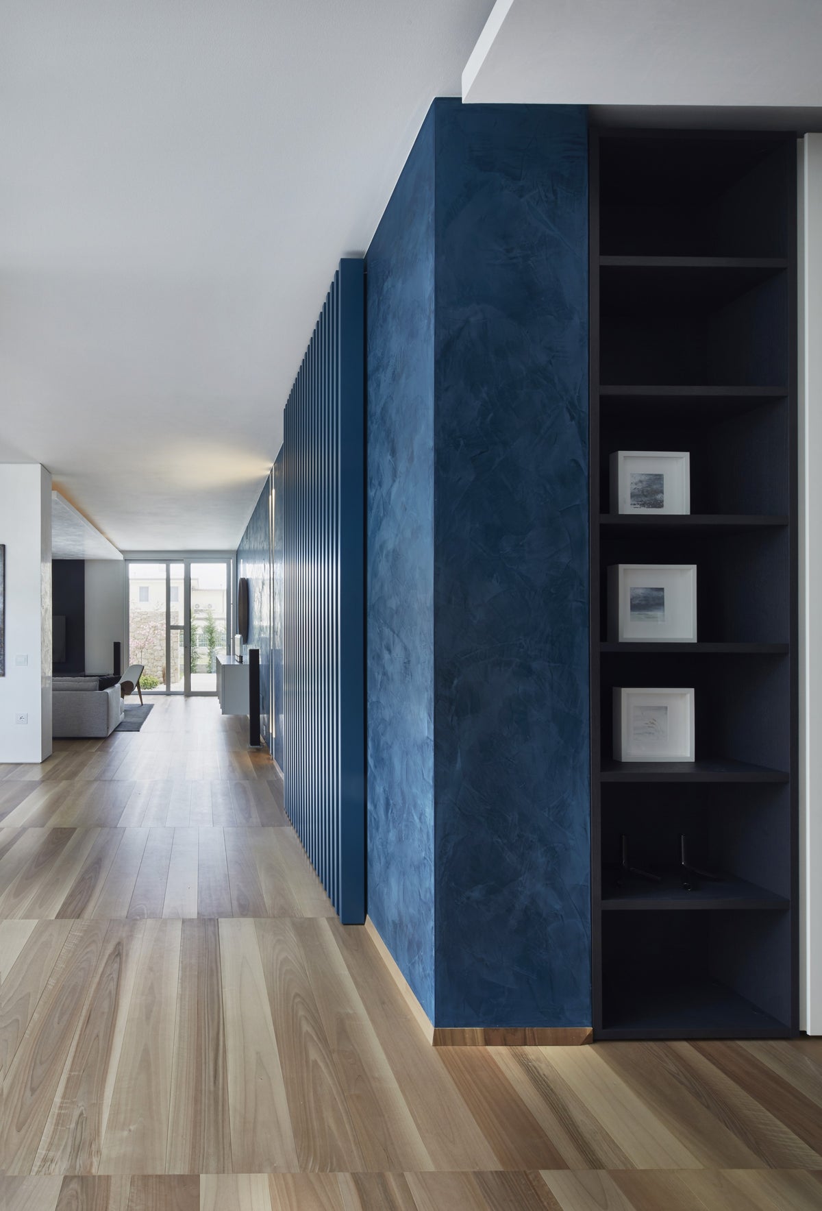 Passaggio con libreria integrata e parete blu, in dialogo con la zona living
