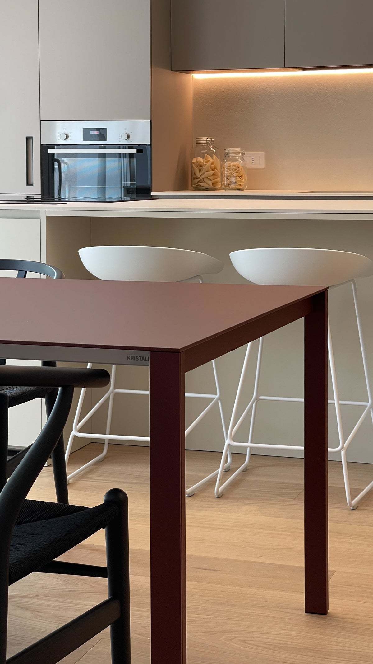 Dettaglio della zona pranzo con tavolo bordeaux e cucina dalle finiture neutre