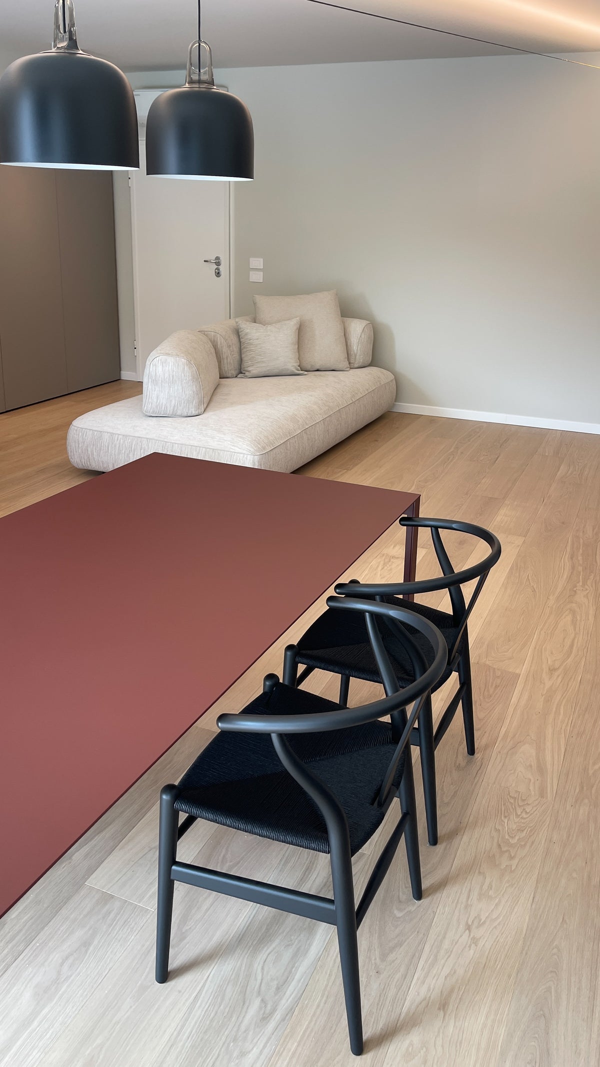 Zona pranzo con tavolo bordeaux, sedie nere e divano chiaro in un open space contemporaneo