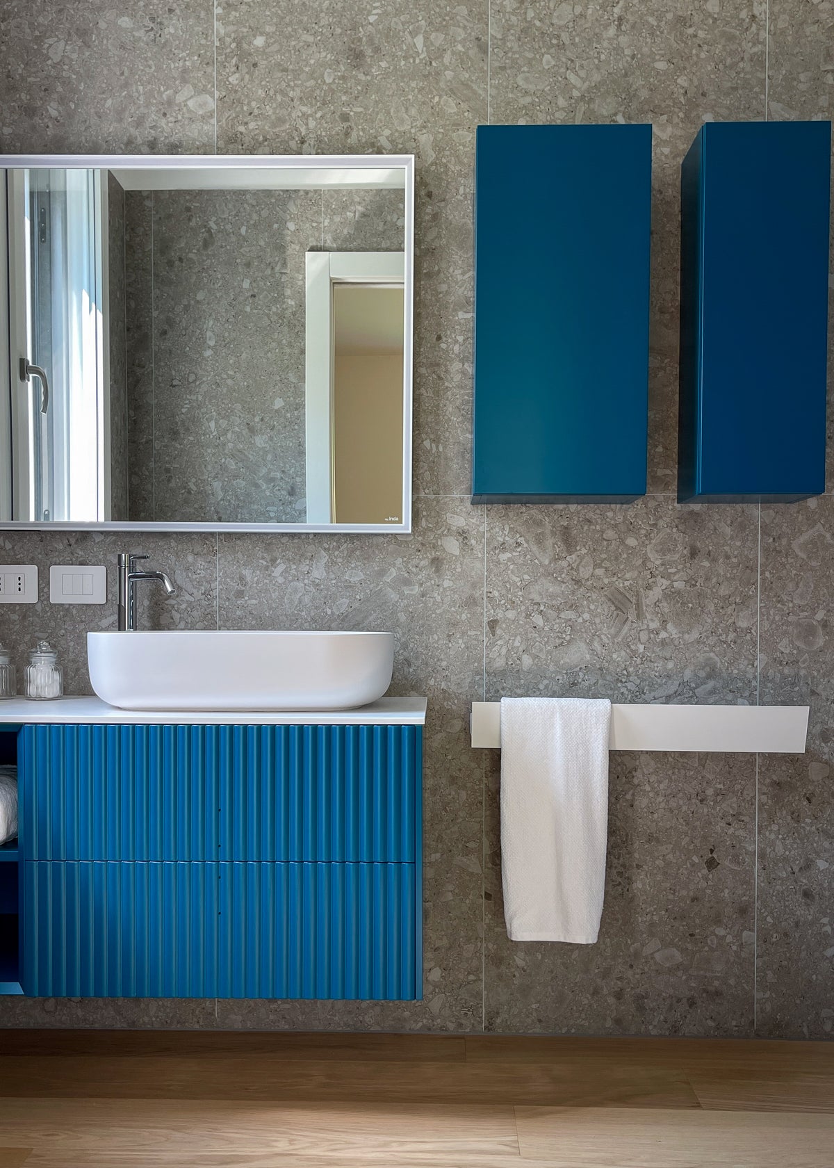 Interior design del bagno con mobile blu ottanio, contenitori sospesi e rivestimento effetto ceppo di gré