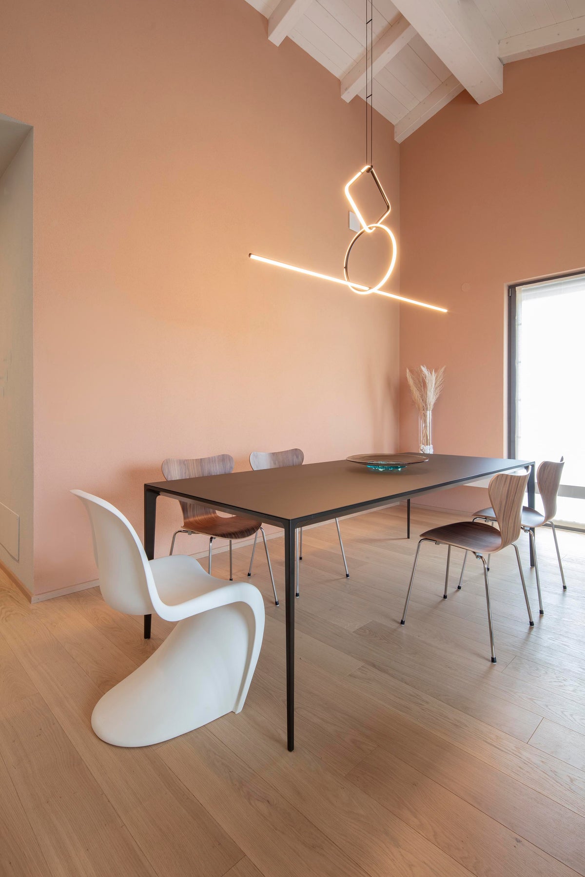 Zona pranzo con parete color cipria, tavolo scuro e illuminazione scenografica