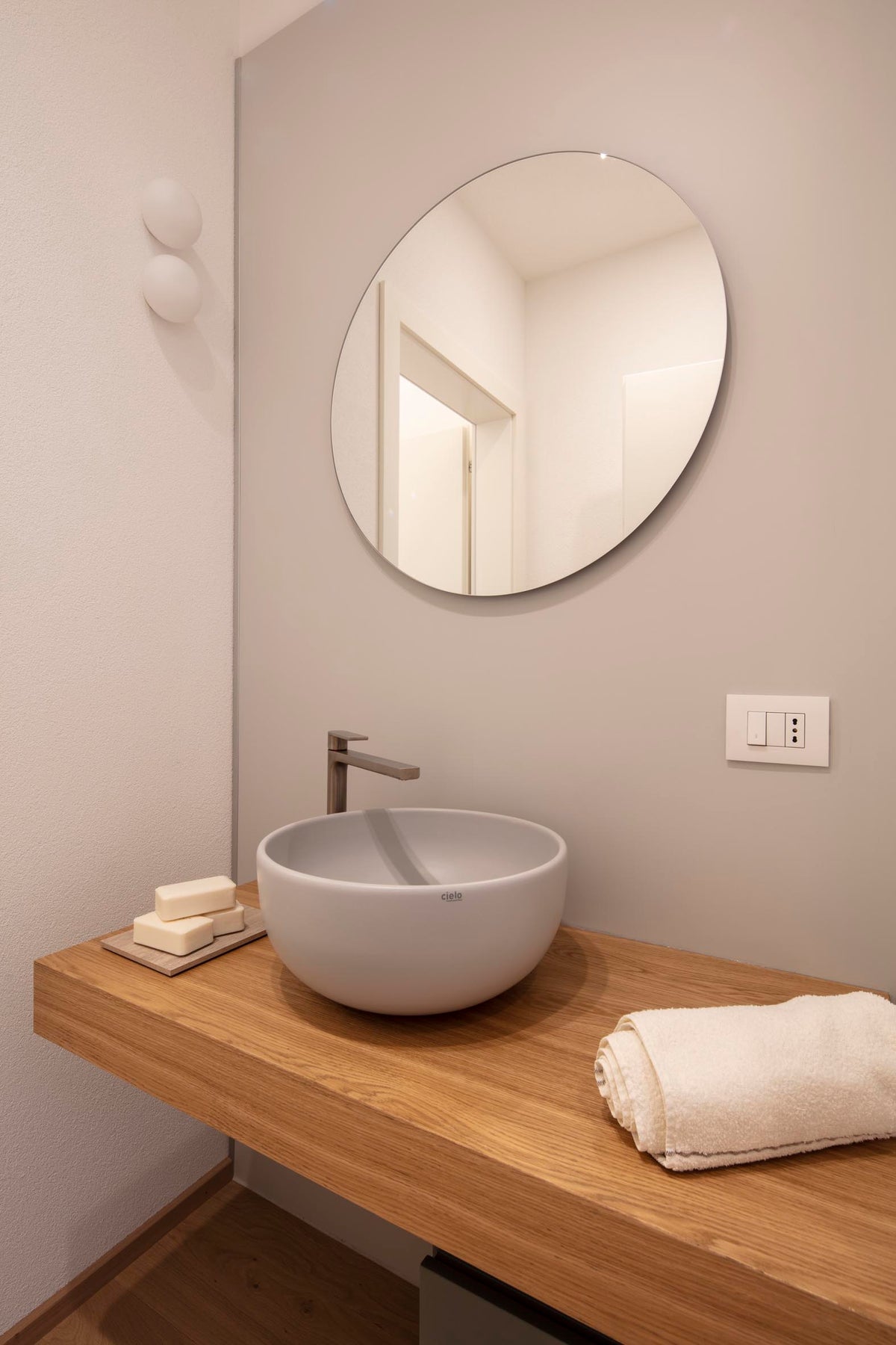 Bagno con lavabo da appoggio, mobile in legno e specchio rotondo