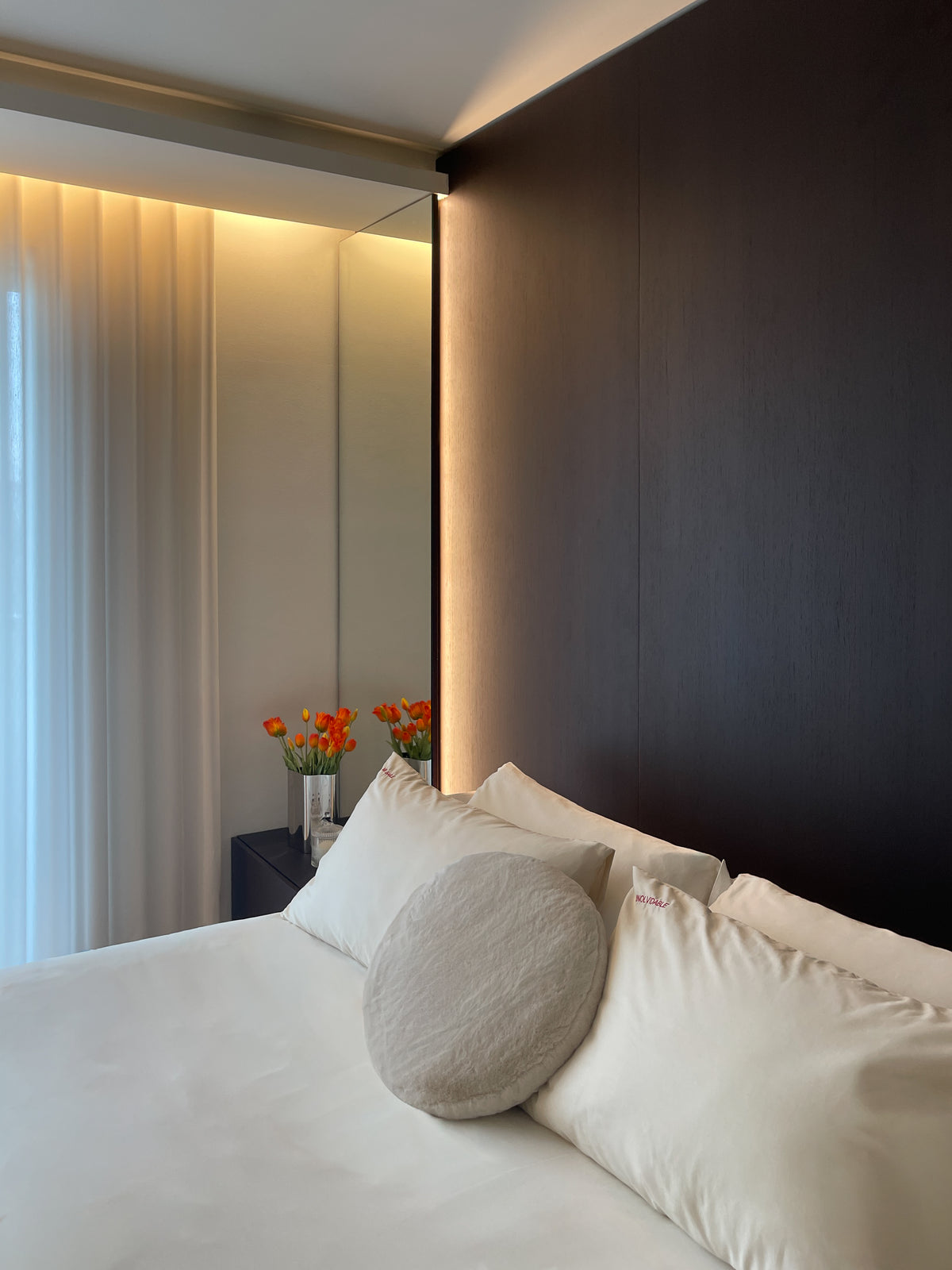 Camera da letto con boiserie in legno scuro, specchio a tutta altezza e illuminazione indiretta
