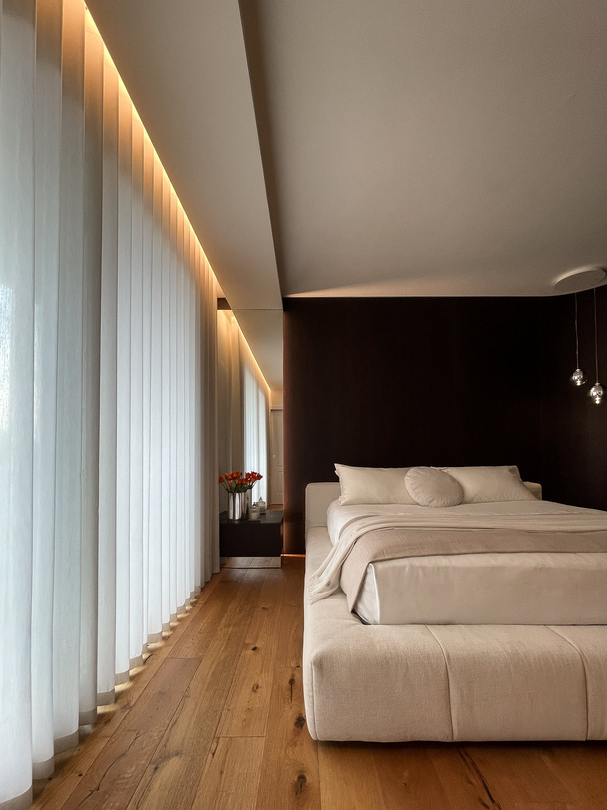 Camera padronale luminosa con letto imbottito, tende a tutta altezza e illuminazione indiretta perimetrale