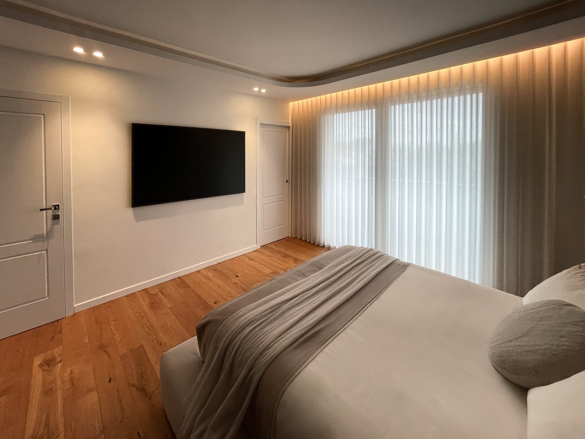 Camera padronale con parete TV, grandi tende filtranti e controsoffitto sagomato con luce indiretta