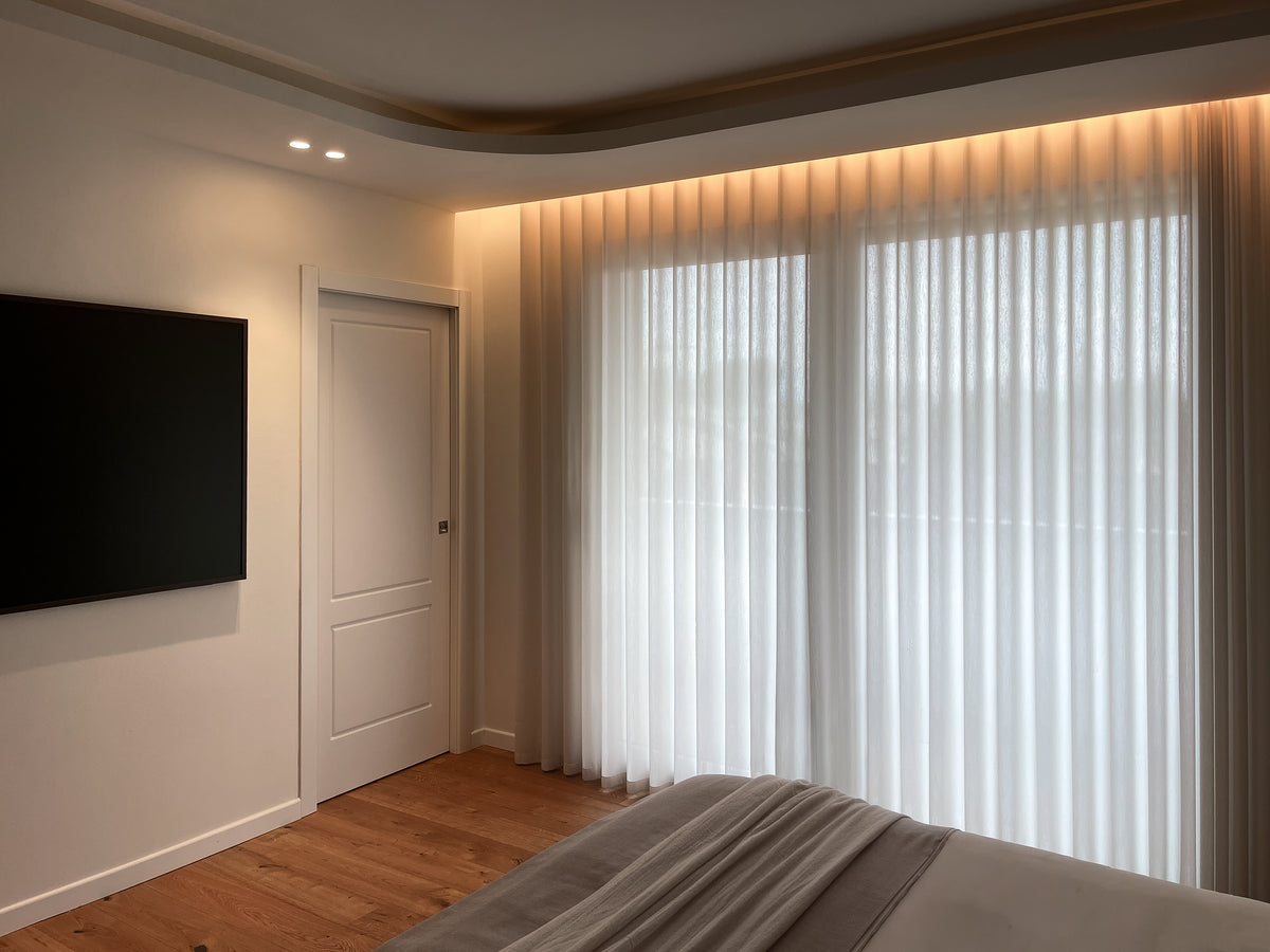 Parete finestrata della camera da letto con tende a tutta altezza e illuminazione indiretta nel controsoffitto