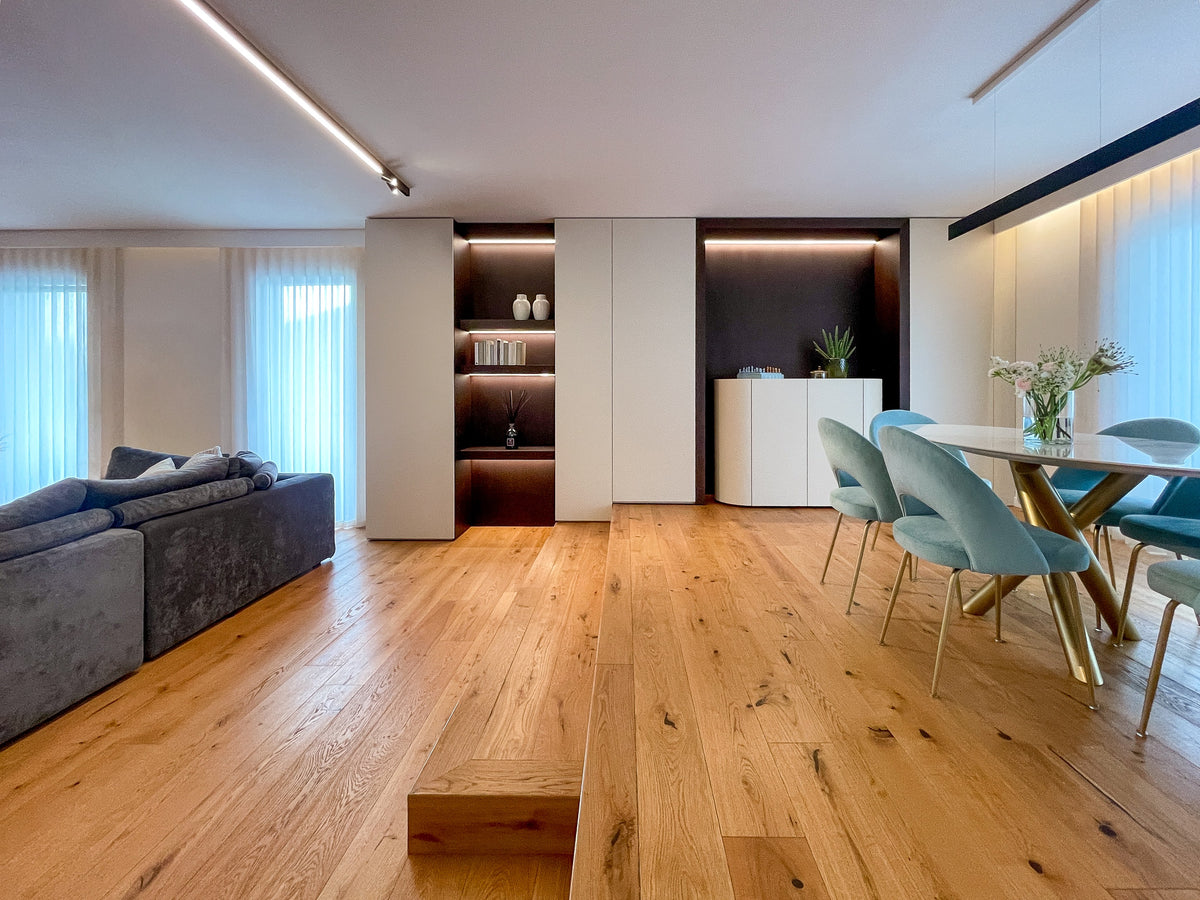 Zona giorno contemporanea con soggiorno e sala da pranzo collegati da arredi su misura e pavimento in legno