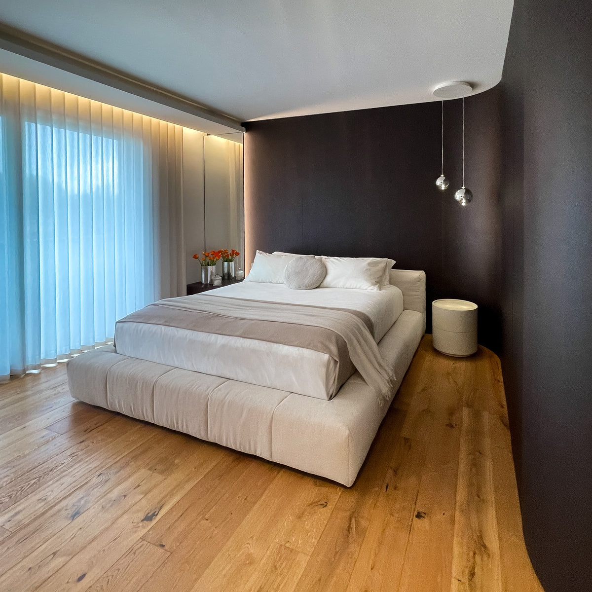 Progetto di interior design con camera padronale contemporanea, dotata di armadiatura curva su misura in legno scuro, letto imbottito e illuminazione integrata