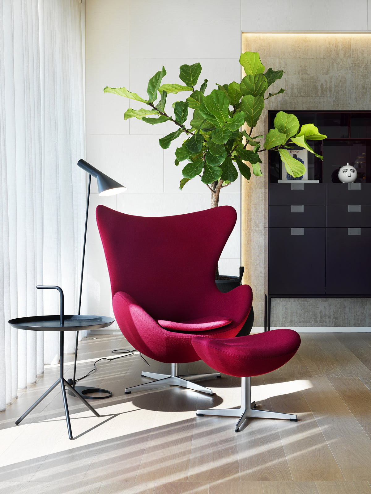 Angolo lettura con poltrona rossa di design con poggiapiedi Fritz Hansen, con lampada da terra, tavolino e pianta verde