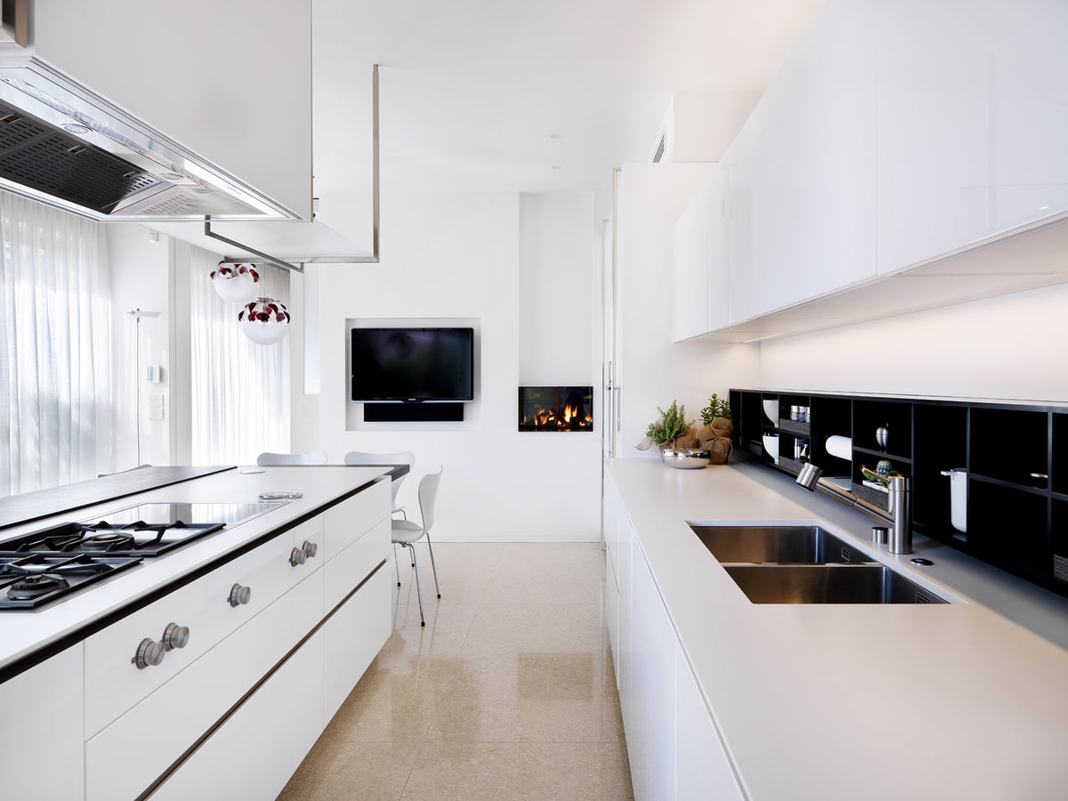 Cucina lineare con finiture bianche e legno scuro, piano cottura doppio a gas e induzione sottotop, lavello integrato