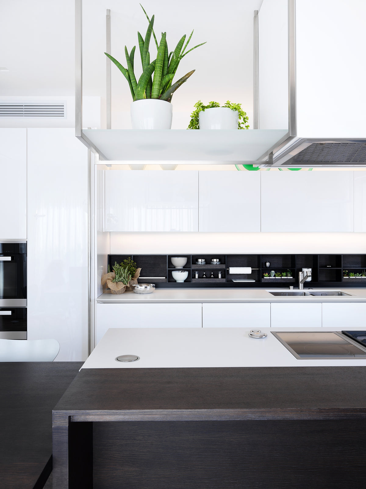 Dettaglio della cucina moderna con pensili minimal, elemento sospeso con cappa e piano cottura sottotop