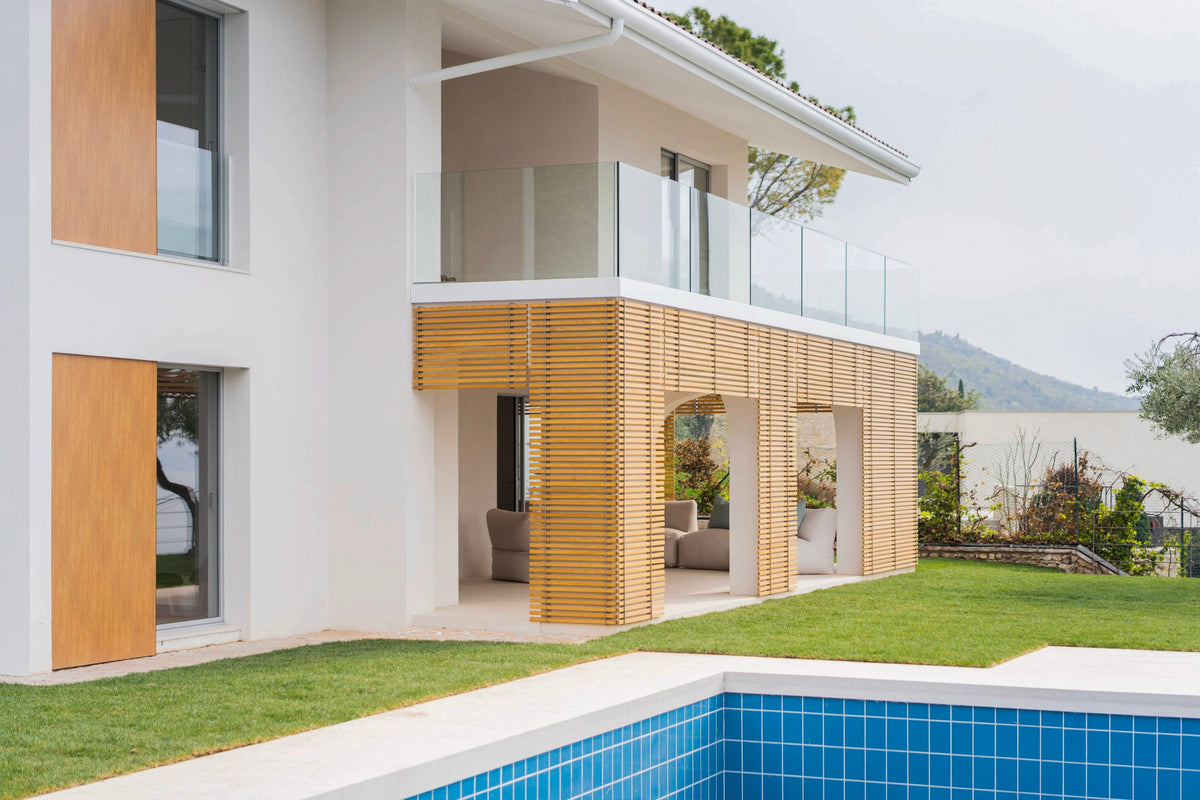 Prospetto della villa con facciata chiara, inserti in legno e piscina panoramica