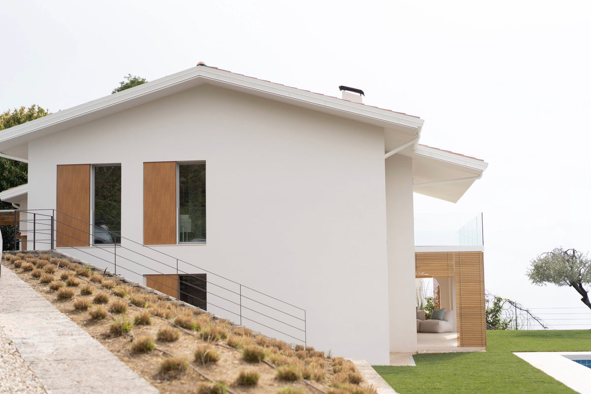 Prospetto laterale della casa con facciata chiara, aperture verticali e giardino