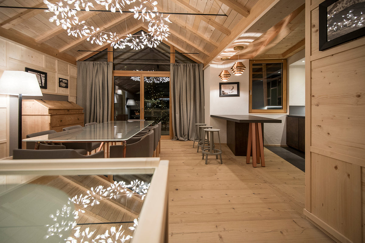 Open space dello Chalet Zeno con cucina in legno, bancone scuro, tavolo conviviale in vetro e illuminazione scenografica