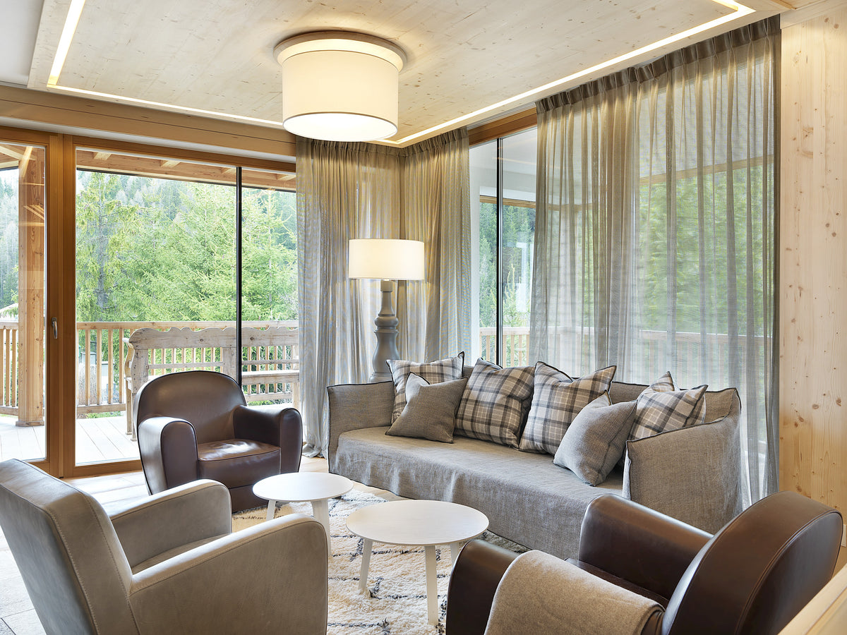 Salotto con arredi comodi e grandi vetrate affacciate sulle Dolomiti, materiali naturali e progetto di interior design per hospitality