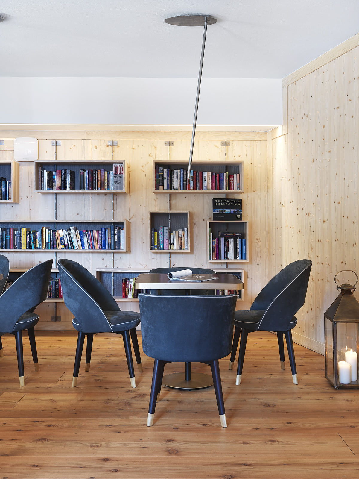Sala lettura con tavoli, libreria a parete e sedute imbottite blu in contrasto con il legno chiaro