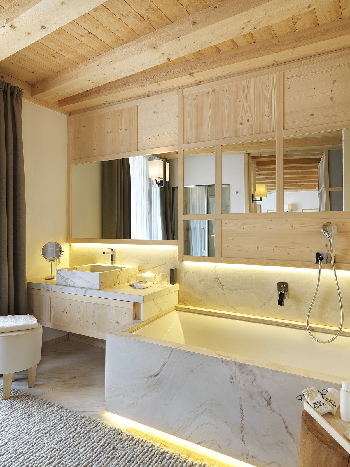 Bagno su misura con lavabo e rivestimenti in pietra, vasca integrata e boiserie in legno in un progetto di interior design per hotel di lusso