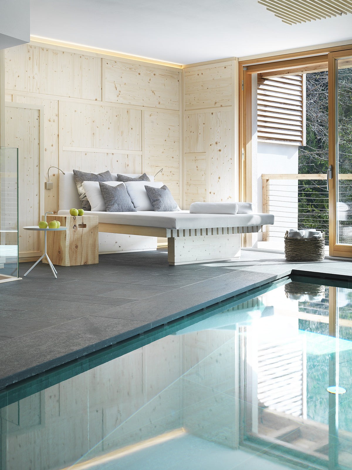 Piscina interna con bordo in pietra e area relax in uno spazio wellness dall’estetica essenziale
