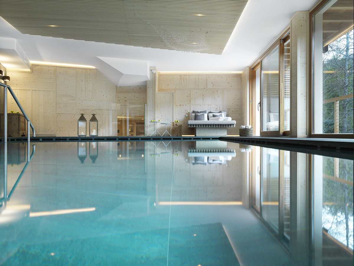 Piscina coperta con superfici chiare, vista sul bosco e luce naturale