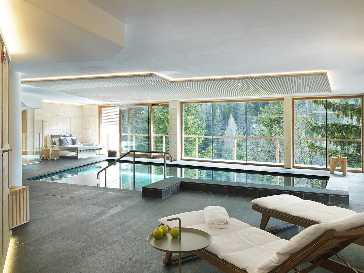 Zona benessere con piscina interna, area lounge e grandi vetrate in un ambiente luminoso e contemporaneo